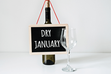 A small chalkboard sign reading Dry January hung on a wine bottle beside an empty wine glass