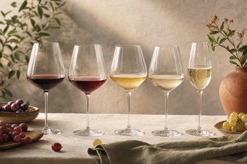 A row of wine glasses from deep red to white to sparkling on cream linen