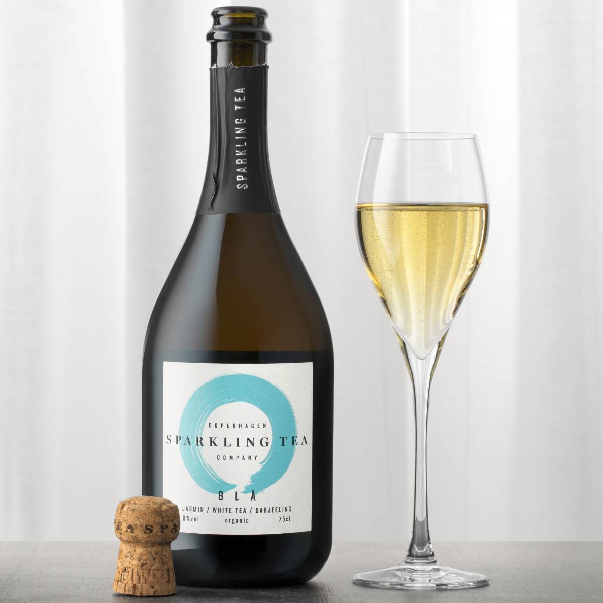 Copenhagen Sparkling Tea BLA opened beside a filled champagne flute, with the cork resting on the table. Producer photography.