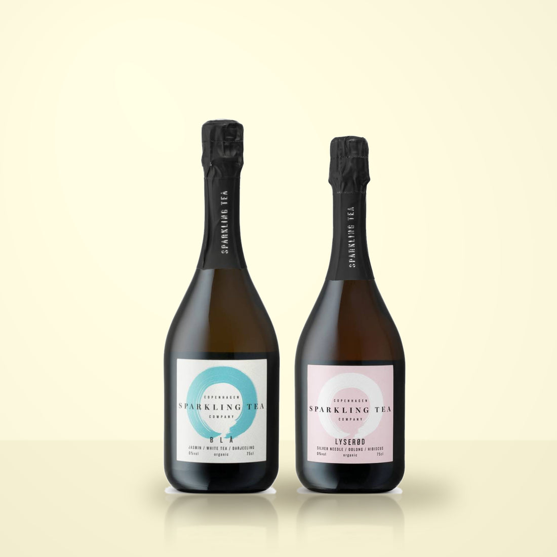 Copenhagen Sparkling Tea BLA and Lyserod bottles side by side on a cream studio background. Both labels read COPENHAGEN SPARKLING TEA COMPANY with 0%vol, organic, 75cl.