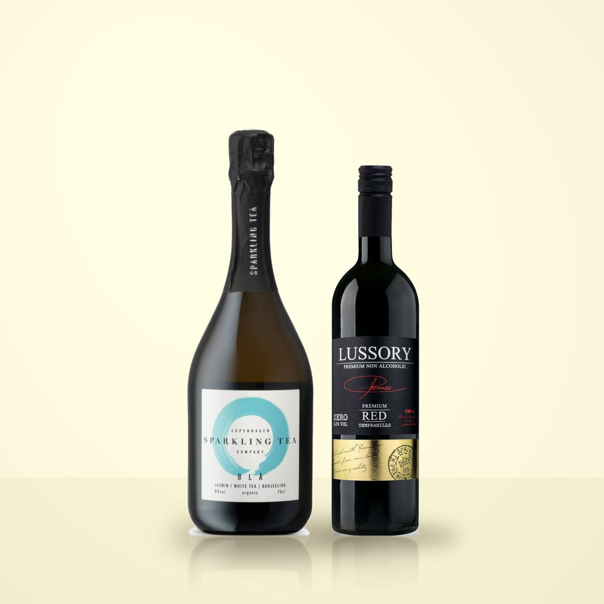 Copenhagen Sparkling Tea BLA beside Lussory Premium Tempranillo on a cream studio background. The Copenhagen label reads 0%vol, organic, 75cl; the Lussory label reads PREMIUM NON ALCOHOLIC and ZERO 0.0% VOL.